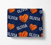 a navy blue blanket with a repeating pattern of orange basketballs and the name "Olivia" written in white.