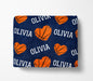 a navy blue blanket with a repeating pattern of orange basketballs and the name "Olivia" written in white.