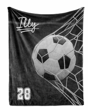 A black and white image of a soccer ball in the net of a soccer goal, with the name "Illy" written above it.