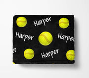 A black blanket with yellow softball images and the name "Harper" written on it in white text.
