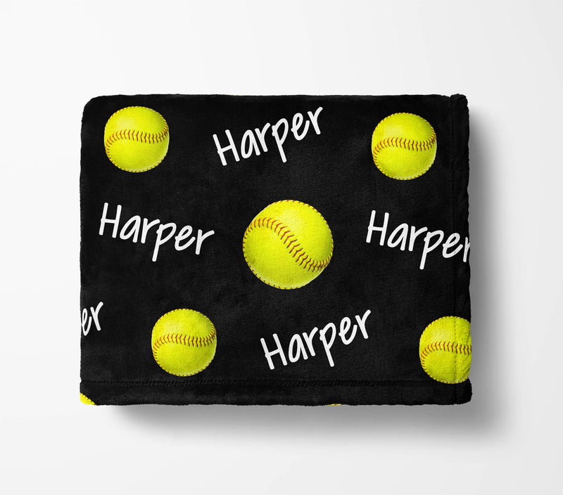A black blanket with yellow softball images and the name "Harper" written on it in white text.