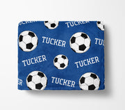 a blue blanket with a repeating pattern of soccer balls and the name "Tucker" printed on it.
