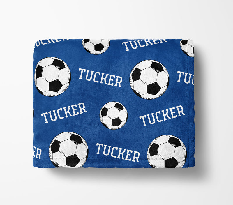 a blue blanket with a repeating pattern of soccer balls and the name "Tucker" printed on it.