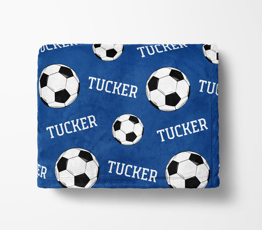 a blue blanket with a repeating pattern of soccer balls and the name "Tucker" printed on it.