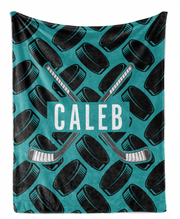 A personalized hockey blanket with a repeating pattern of hockey sticks crossed over each other and the name "Caleb" printed on it.