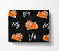 a black blanket with a repeating pattern of orange cheerleading pom-poms and the name "Lily" written in white.
