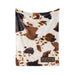 a blanket with a cow print pattern, and there is a small patch on the blanket with the word "NOTEBOOM" printed on it.
