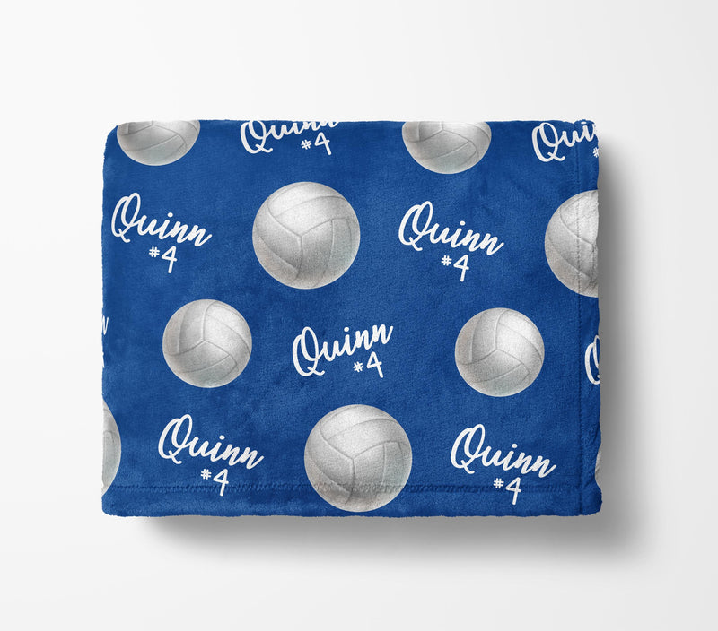 a blue blanket with a repeating pattern of volleyball images and the name "Quinn #4" printed on it.