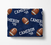 a navy blue blanket with a repeating pattern of footballs and the name "Cameron #99" printed on it.