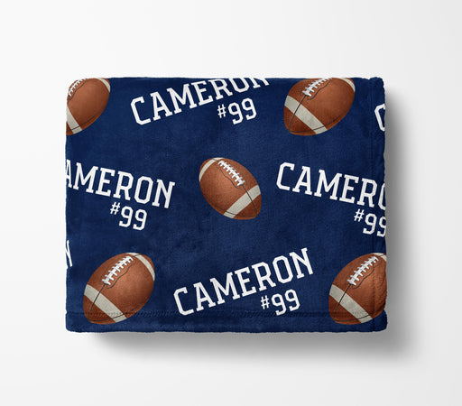 a navy blue blanket with a repeating pattern of footballs and the name "Cameron #99" printed on it.