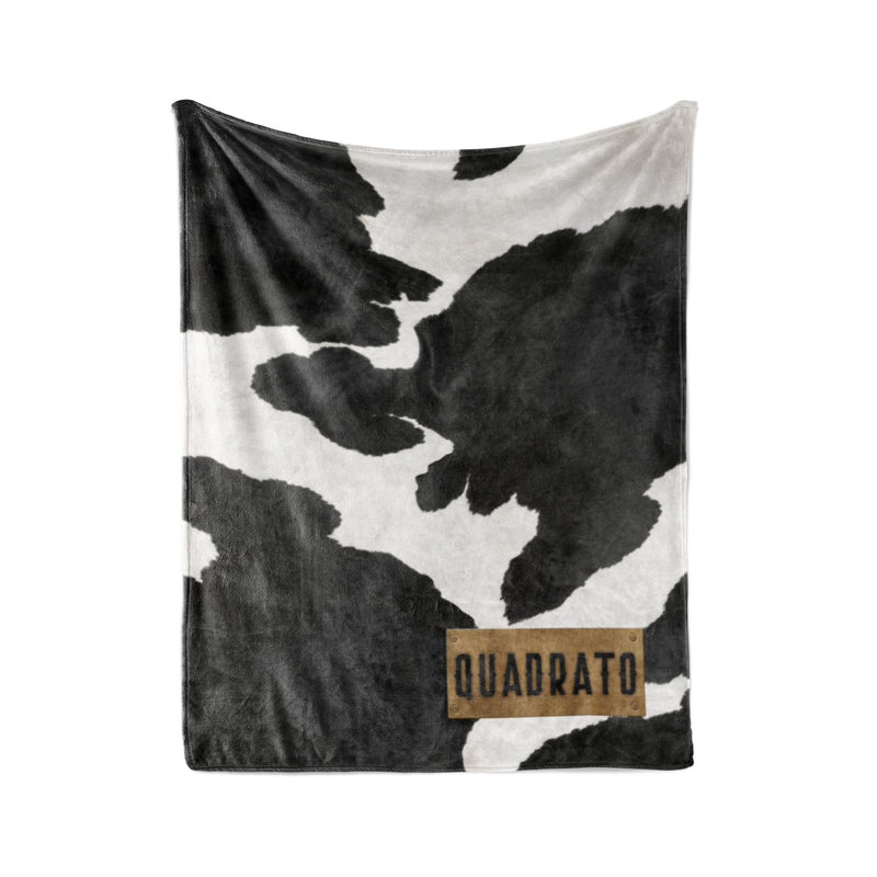 a black and white cow print blanket with the word "QUADRATO" printed on it.
