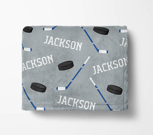 A gray blanket with a repeating pattern of hockey sticks and a puck, along with the name "JACKSON" printed on it.
