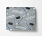 A gray blanket with a repeating pattern of hockey sticks and a puck, along with the name "JACKSON" printed on it.