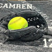 A black and white image of a baseball glove with a yellow softball inside it, along with the text "CAMREN" and the number "12" in the background.