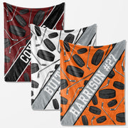 three square-shaped blankets with a repeating pattern of hockey sticks and puck images. The blankets are in different colors: red, white, and orange.