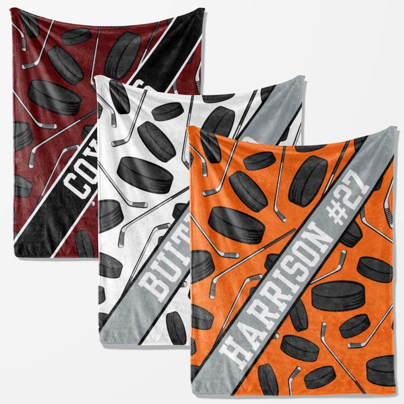 three square-shaped blankets with a repeating pattern of hockey sticks and puck images. The blankets are in different colors: red, white, and orange.