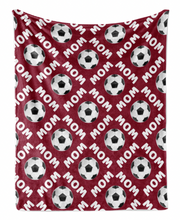 a red blanket with a repeating pattern of soccer balls and the word "MOM" printed on it.