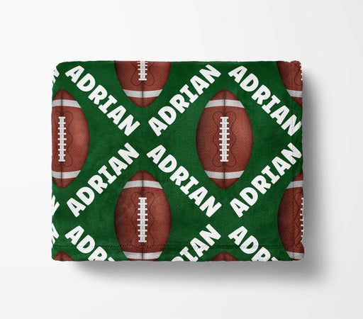 a green blanket with a repeating pattern of red footballs and the name "ADRIAN" written in white.