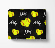 A black blanket with a repeating pattern of yellow softball hearts and the name "Abby" written in white.