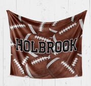 A brown blanket with white footballs printed on it, and the name "Holbrook" written across it.