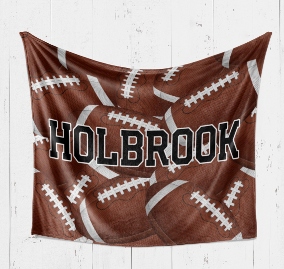 A brown blanket with white footballs printed on it, and the name "Holbrook" written across it.