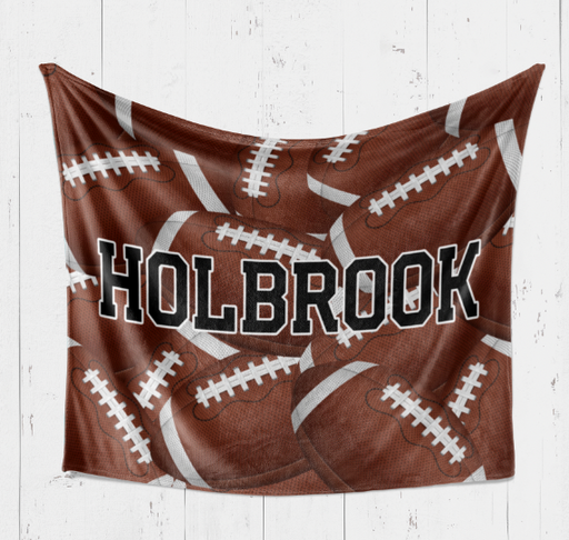 A brown blanket with white footballs printed on it, and the name "Holbrook" written across it.