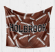 A brown blanket with white footballs printed on it, and the name "Holbrook" written across it.
