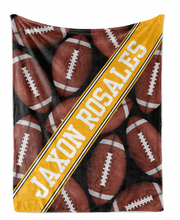 A blanket with a repeating pattern of footballs in various shades of brown and white, with the name "JAXON ROSALES" printed in bold yellow letters diagonally across the blanket.