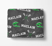 a gray blanket with a repeating pattern of green lacrosse equipment and the word "MACLAIN" printed on it.