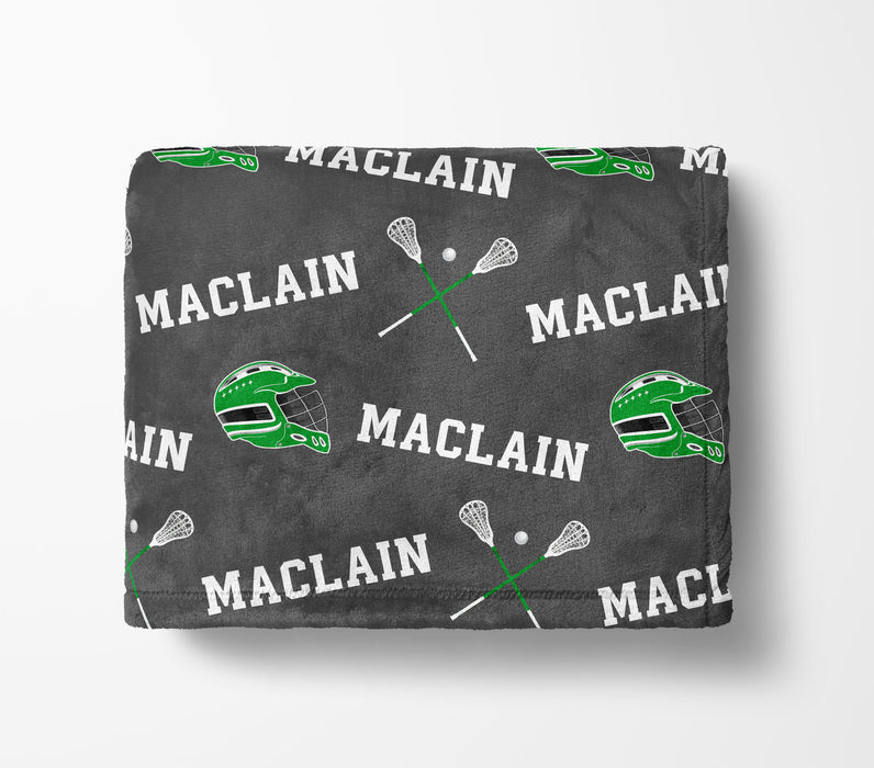 a gray blanket with a repeating pattern of green lacrosse equipment and the word "MACLAIN" printed on it.