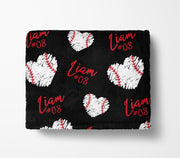 a black blanket with a repeating pattern of white baseball hearts and the name "Liam" written in red cursive.
