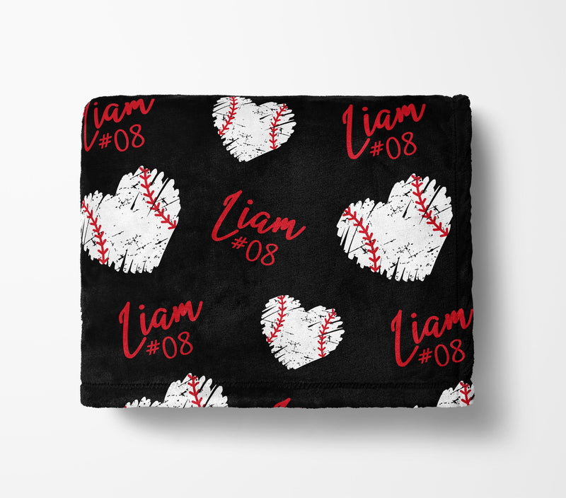 a black blanket with a repeating pattern of white baseball hearts and the name "Liam" written in red cursive.