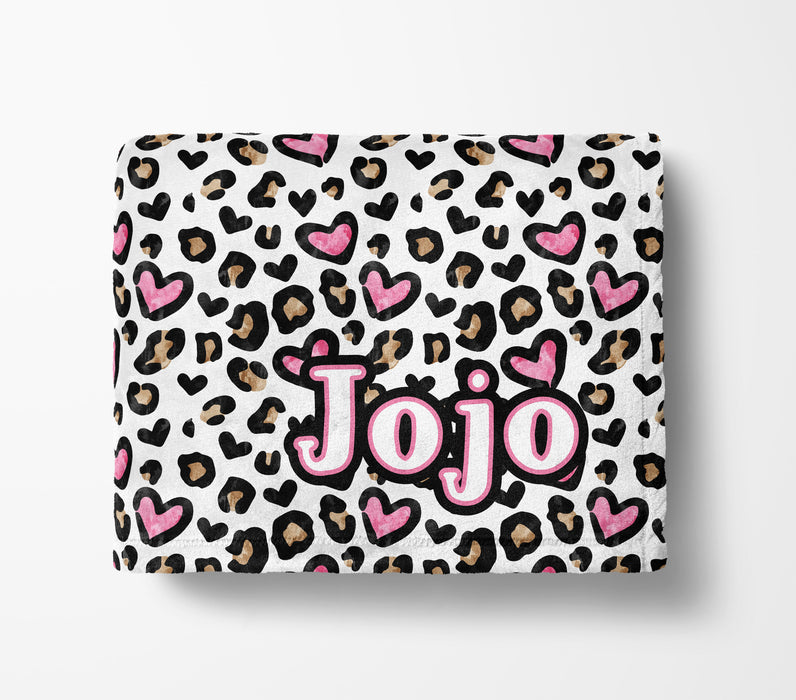 A white blanket with a leopard print pattern and pink hearts. The word "Jojo" is written in pink letters on the blanket.