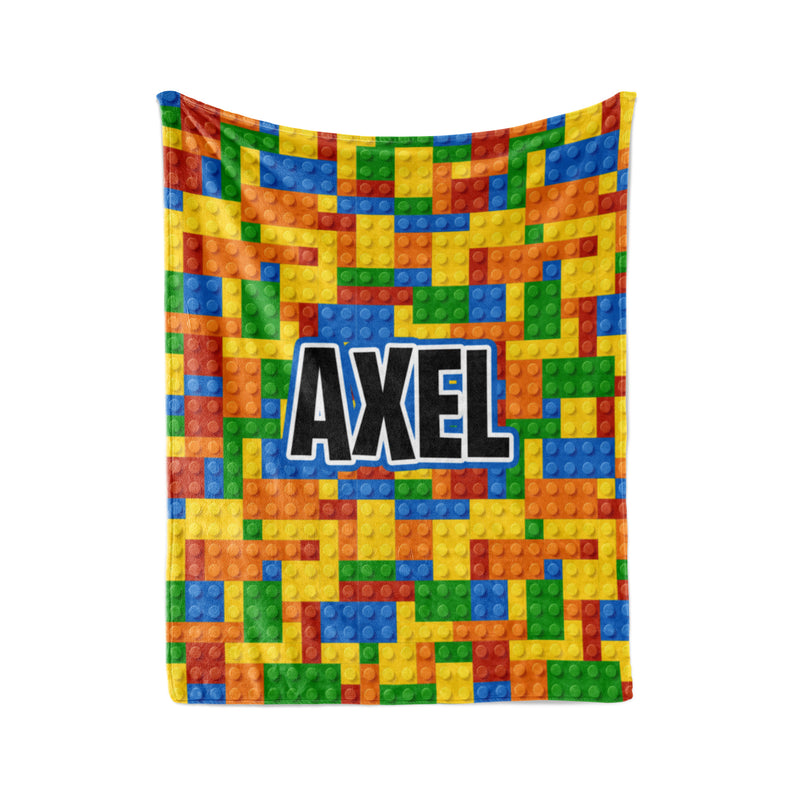 A colorful blanket with a pattern of building blocks in various colors, including red, yellow, green, blue, and orange. The word "AXEL" is prominently displayed in the center of the blanket.