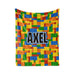 A colorful blanket with a pattern of building blocks in various colors, including red, yellow, green, blue, and orange. The word "AXEL" is prominently displayed in the center of the blanket.