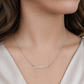 A close-up of a woman wearing a delicate silver chain necklace with a personalized nameplate that reads 'Jaiden' in cursive script, accompanied by a small heart at the end.